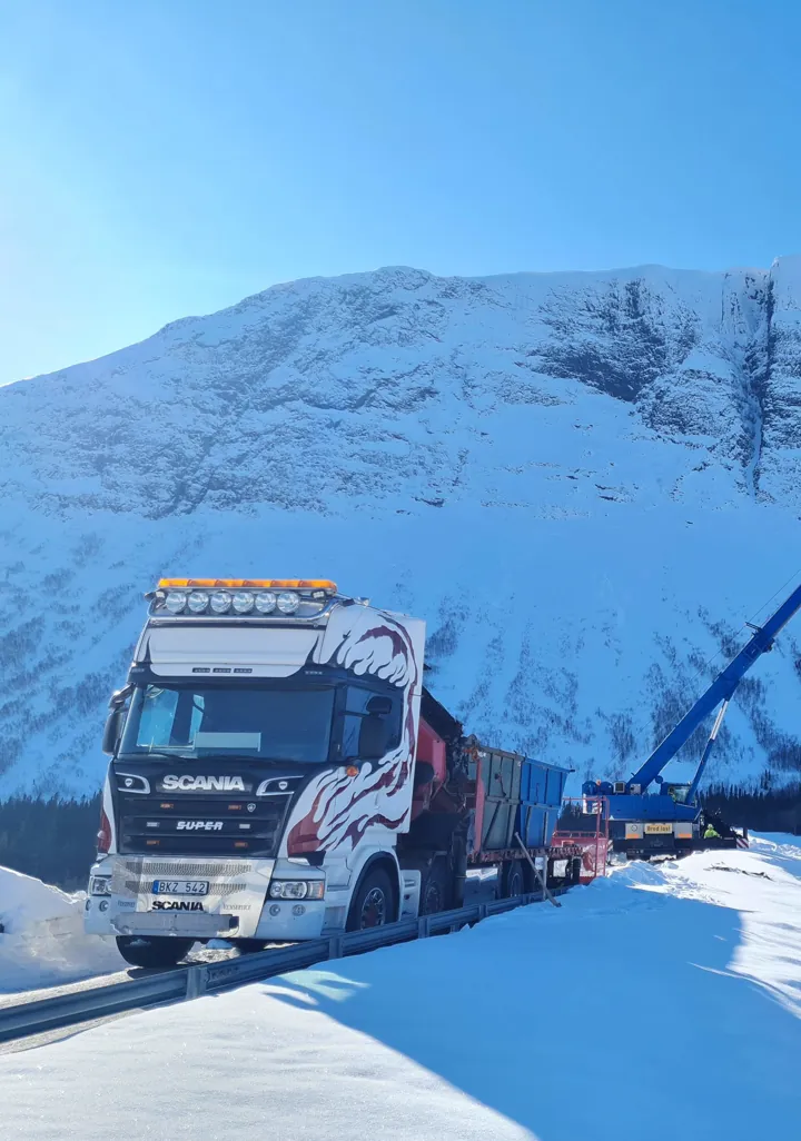 Scania-kranbil och mobilkran på uppdrag framför ett snötäckt fjäll